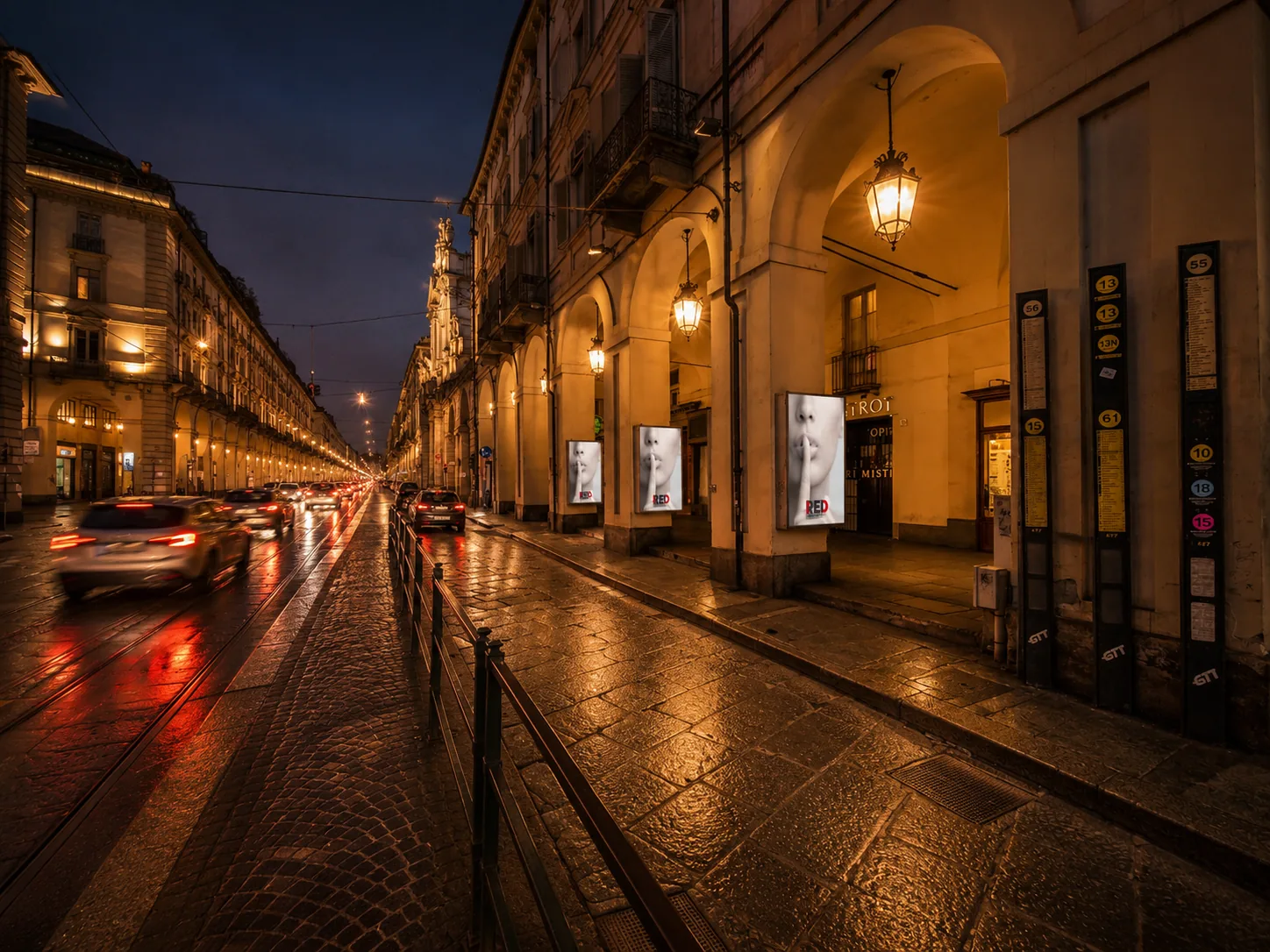 Vetrine pubblicitarie retroilluminate accese sotto i portici di via Po a Torino, in una sera dopo la pioggia
